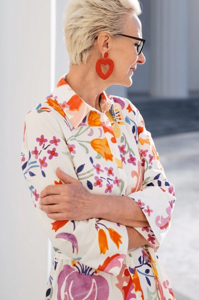 femme mature aux cheveux blancs et veste fleurie colorée, moderne, elle porte de grosses boucles d'oreilles