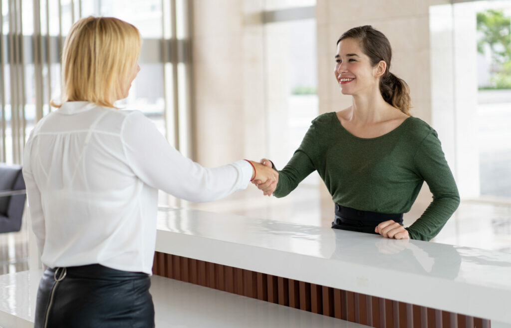 Réceptionniste en entreprise serrant la main d'une cliente au dessus d'un comptoir